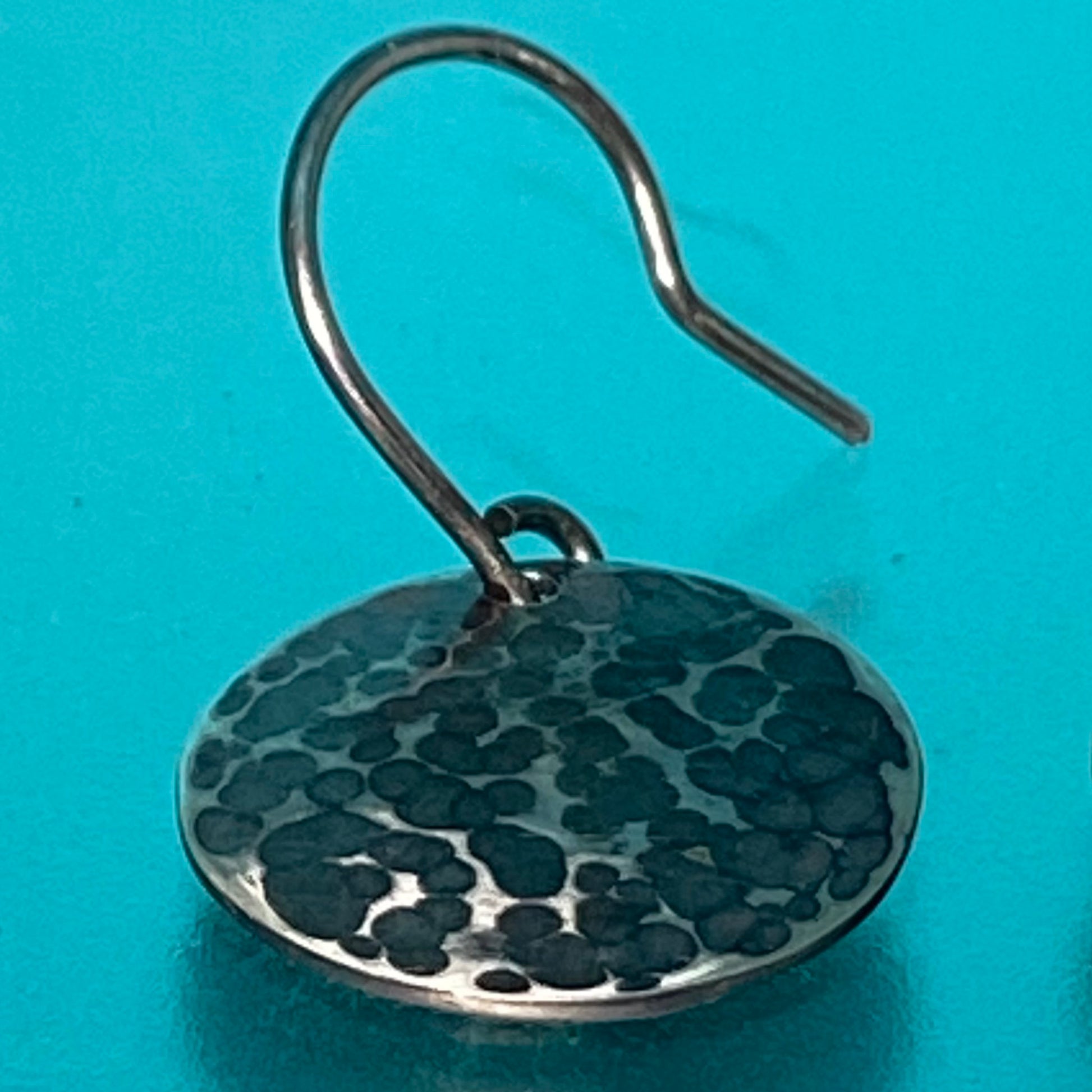 Arete de Plata Fina 950, Joyas de Tendencia. Primerísimo plano del diseño circular martillado y oxidado sobre fondo azul vibrante (Barranquilla).