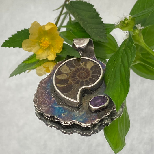 Dije de Plata Fina 950 con Estilo Bohemio, diseño de hoja realizado con técnica de casting (fundición). Primer plano sobre superficie reflectante con fondo claro, acompañado de una piedra y hoja verde (Pereira).