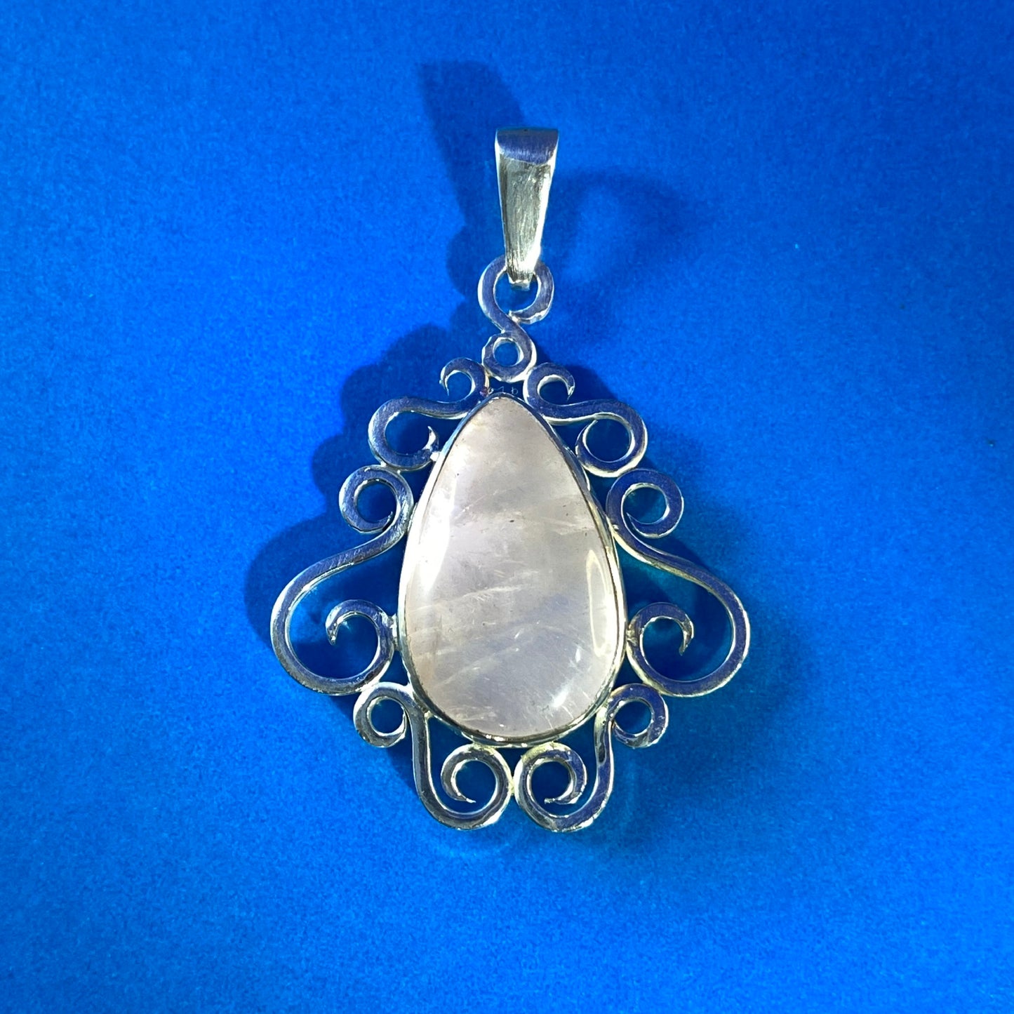 Dije de Plata Pura 950. Colgante con cuarzo rosado en engaste de volutas, sobre fondo azul semi reflectante.