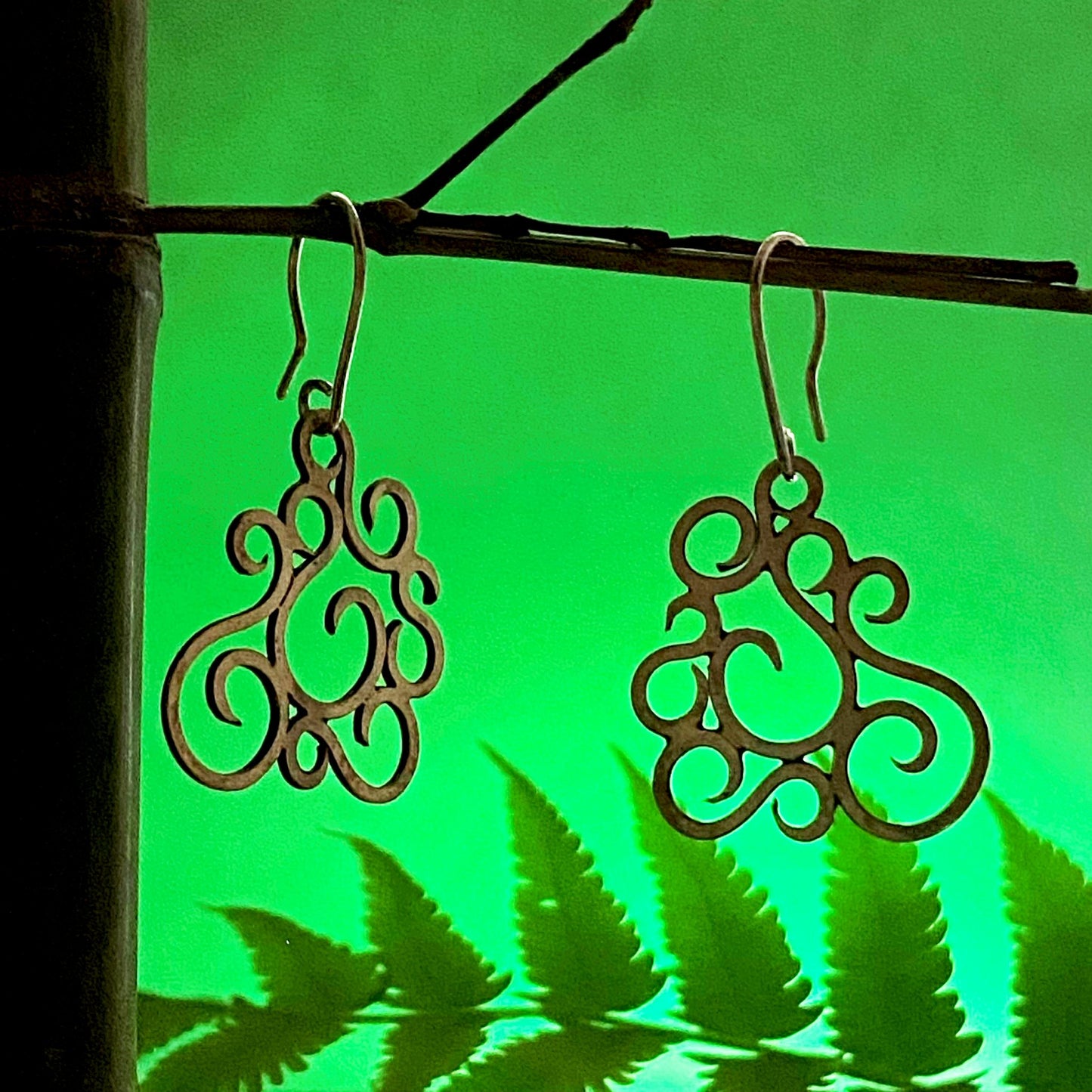 Aretes de Plata Fina 950 con Inspiración en la Naturaleza. Diseño dramático, mostrando la joya colgando de un bambú con una hoja de helecho a contraluz con fondo verde (Buenaventura).