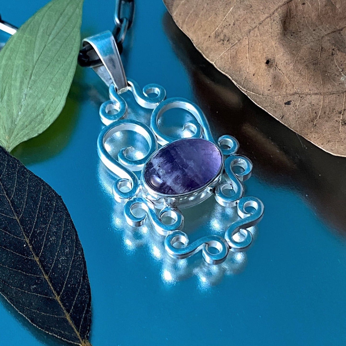 Dije de Plata Fina 950 (Colombia). El colgante con Amatista es realzado con decoración de hojas secas y frescas sobre fondo azul metálico.