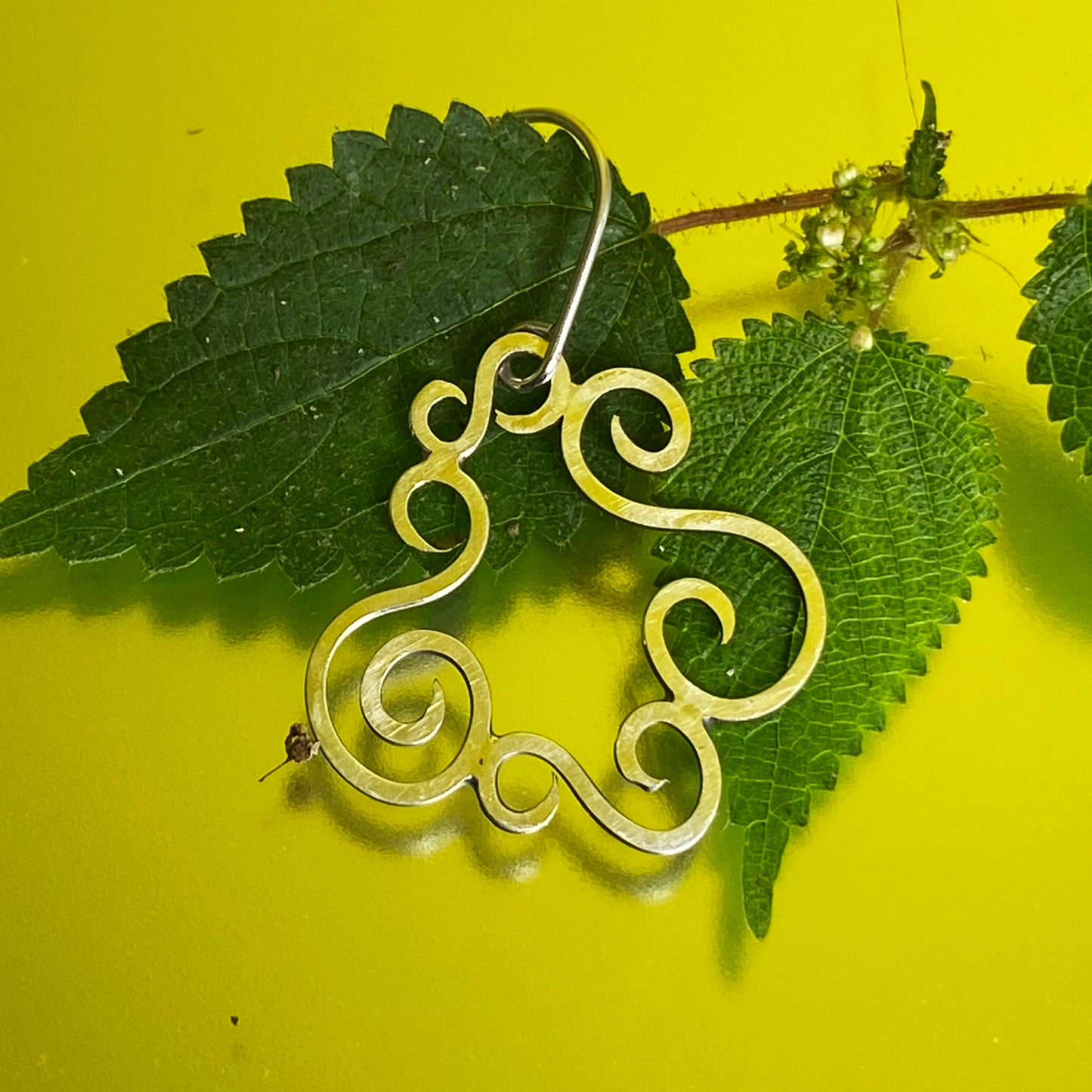 Primer plano de un solo Arete de Plata Fina 950 de Pieza Original. La joya está posada sobre hojas de monte con fondo amarillo.