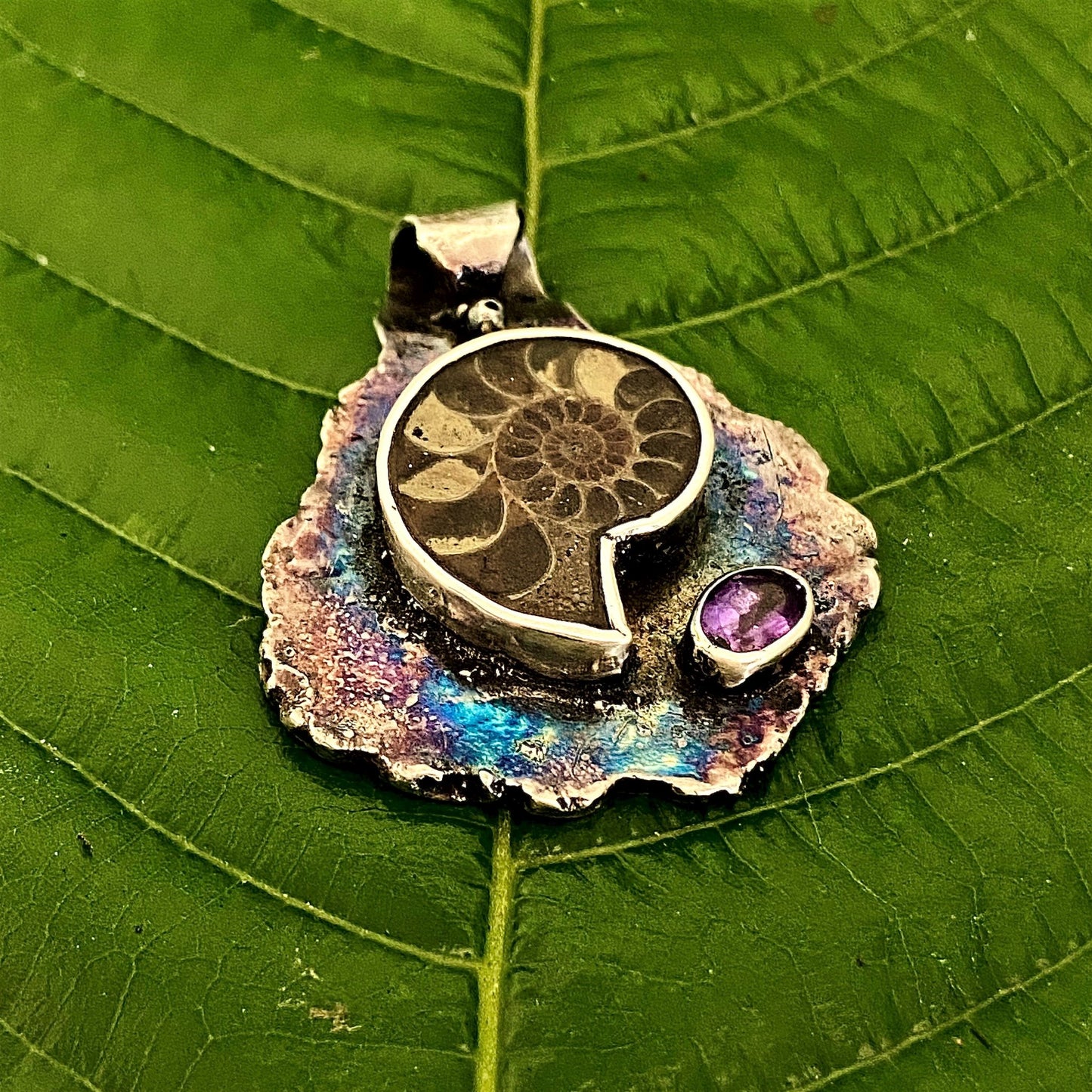 Dije de hoja de Plata Fina 950 de Colombia. Primer plano del colgante oxidado con textura de vena, pieza original con reflejo sobre superficie clara.