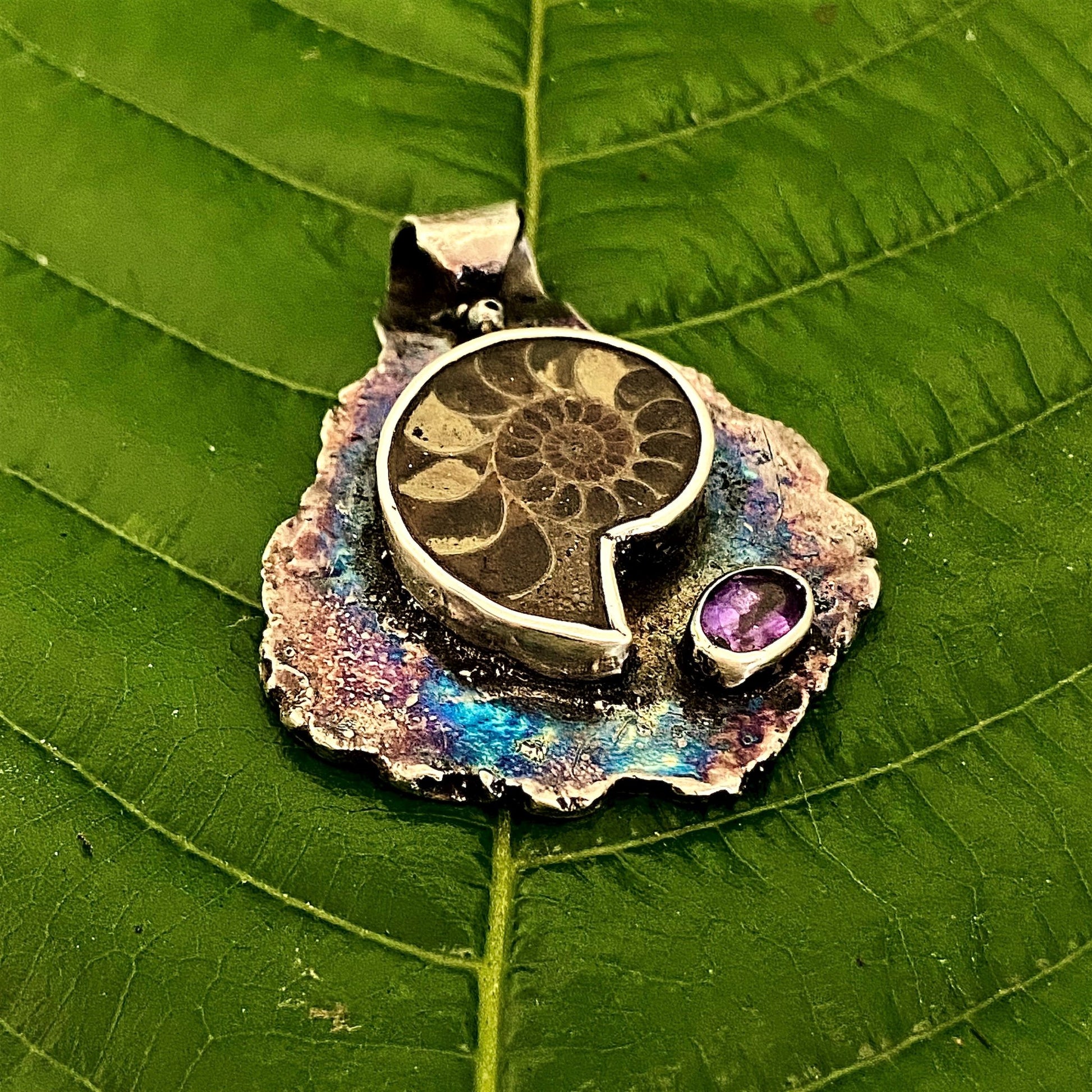 Dije de hoja de Plata Fina 950 de Colombia. Primer plano del colgante oxidado con textura de vena, pieza original con reflejo sobre superficie clara.