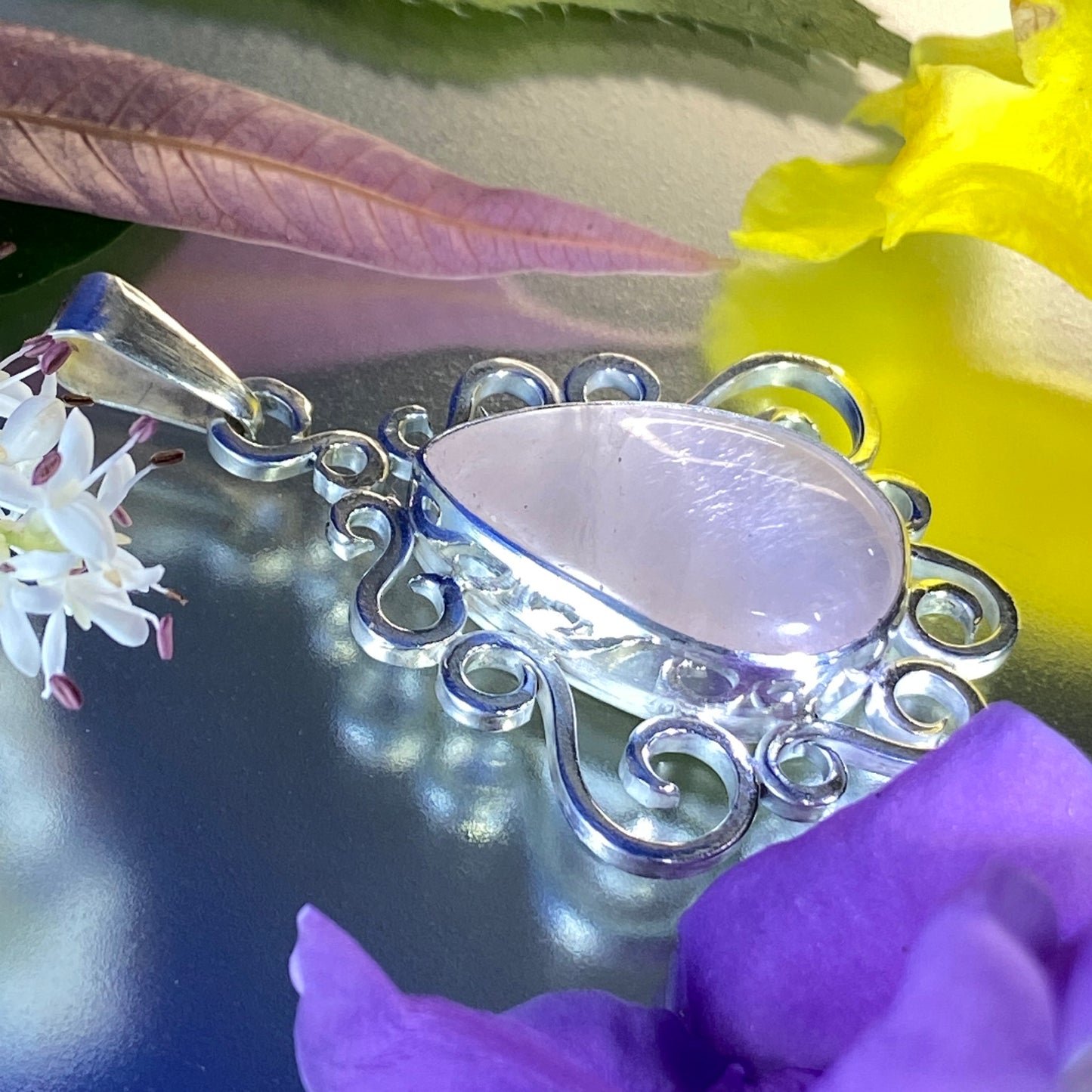 Unique Handcrafted Jewelry (Joyería Hecha a Mano). Dije de Plata 950 y Cuarzo Rosado. Vista lateral. Sobre superficie muy brillante. Destaca la gema y la textura de una hoja que se secó rosada.