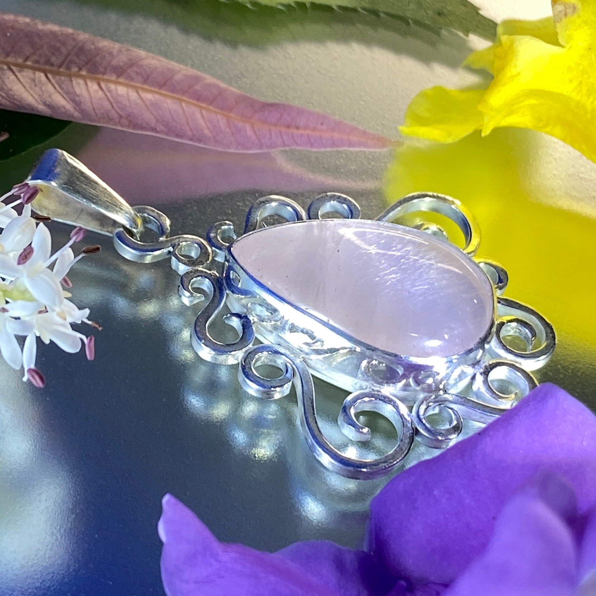 Unique Handcrafted Jewelry (Joyería Hecha a Mano). Dije de Plata 950 y Cuarzo Rosado. Vista lateral. Sobre superficie muy brillante. Destaca la gema y la textura de una hoja que se secó rosada.