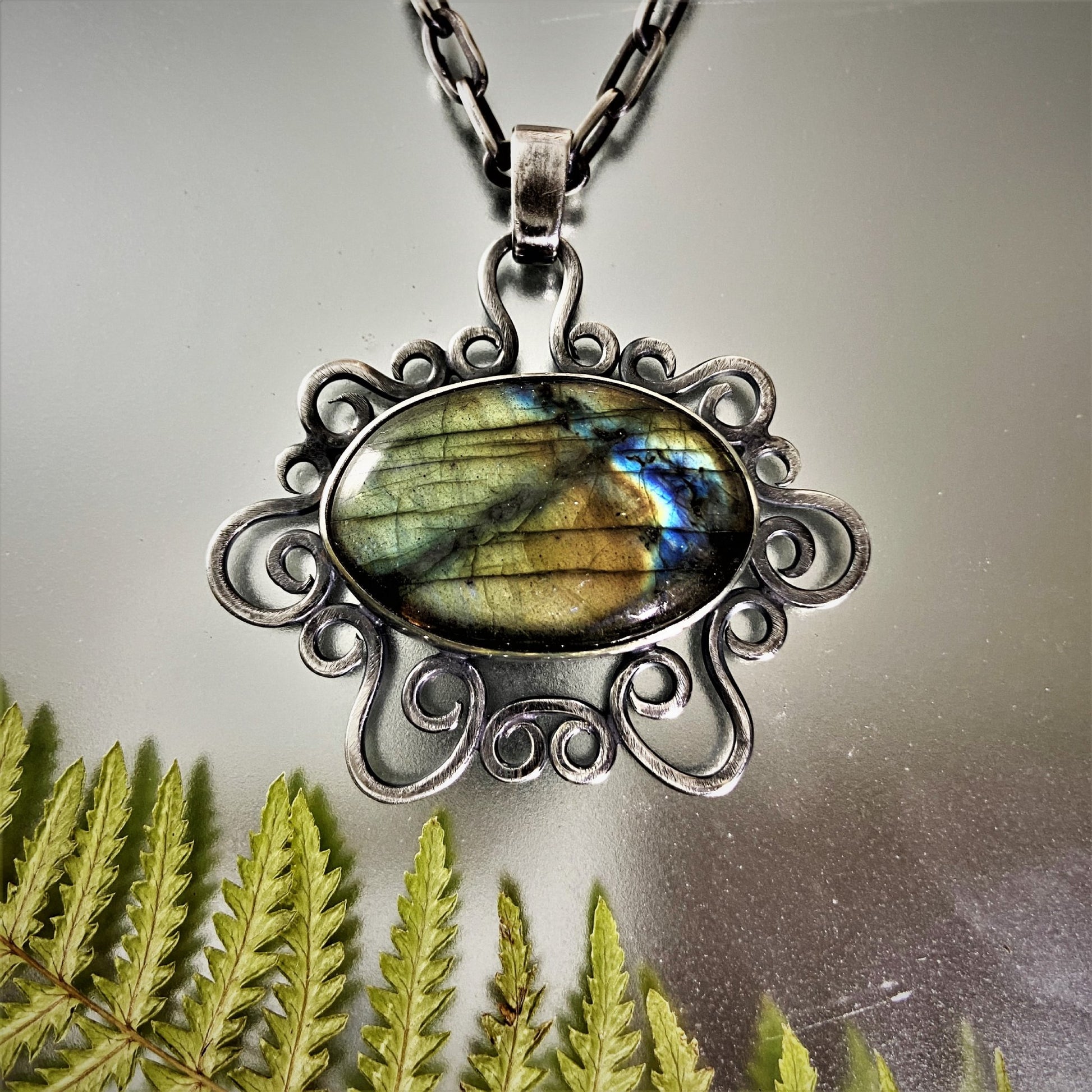 Colombian Jewelry. Dije de Cuarzo Rosado en marco de volutas. Decoración conhelecho, destacando el acabado de la plata sobre fondo reflectante.