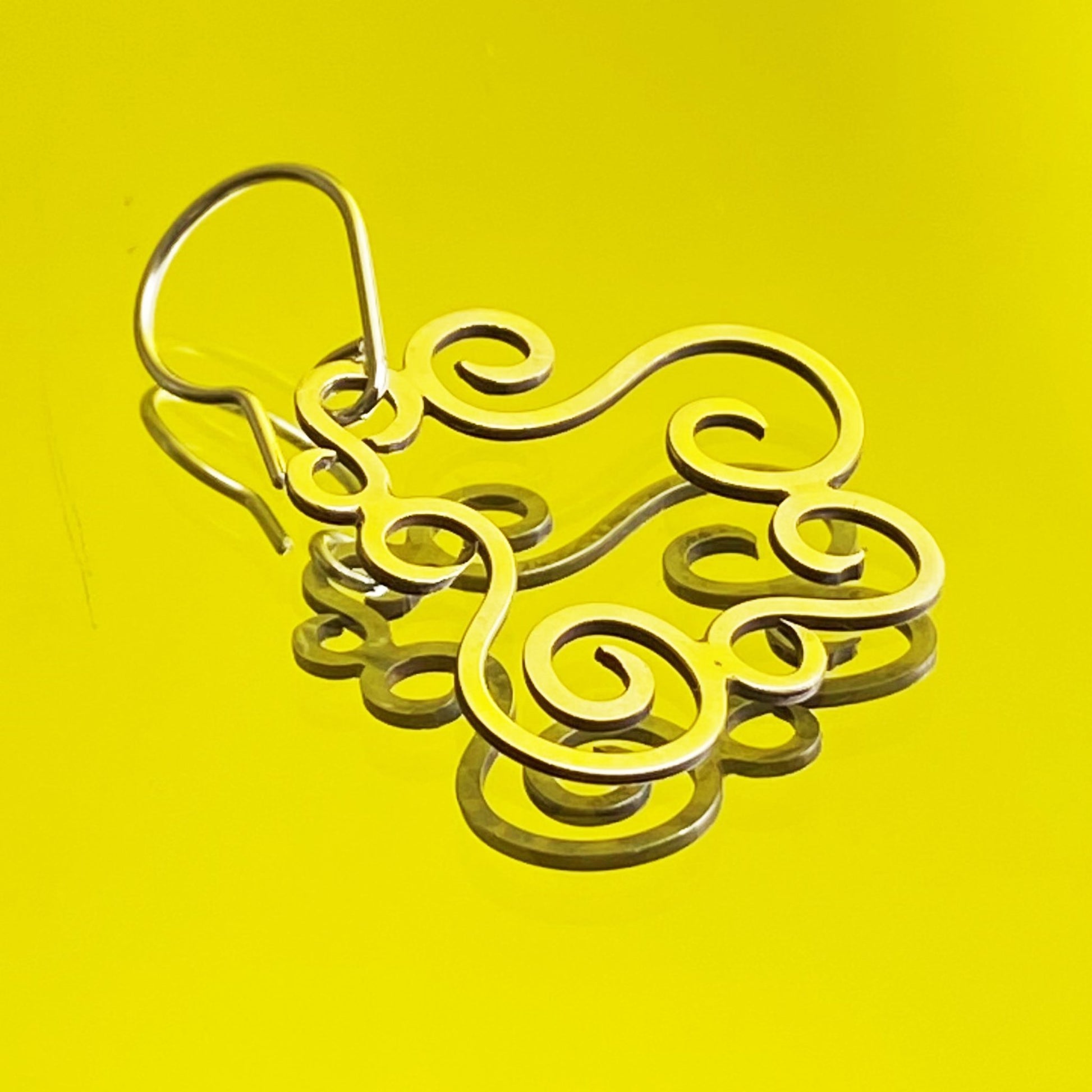 Diseño Minimalista en Plata Fina 950. La pieza, de estilo orgánico, se presenta en primer plano sobre una superficie de espejo reflectante con un intenso fondo amarillo.