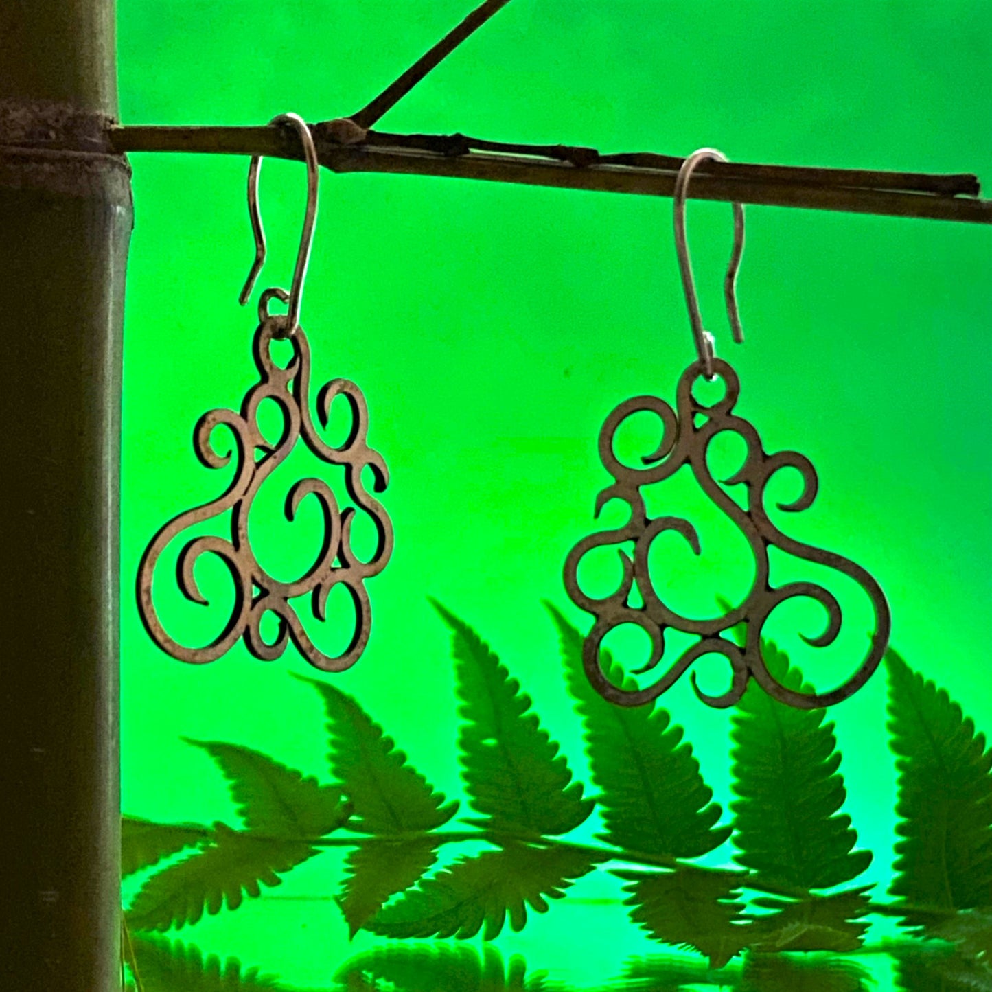Aretes de Plata Fina 950 Hechos a Mano (Medellín). Muestra la pieza con mayor iluminación sobre la vara de bambú, reduciendo el contraste con el fondo verde.